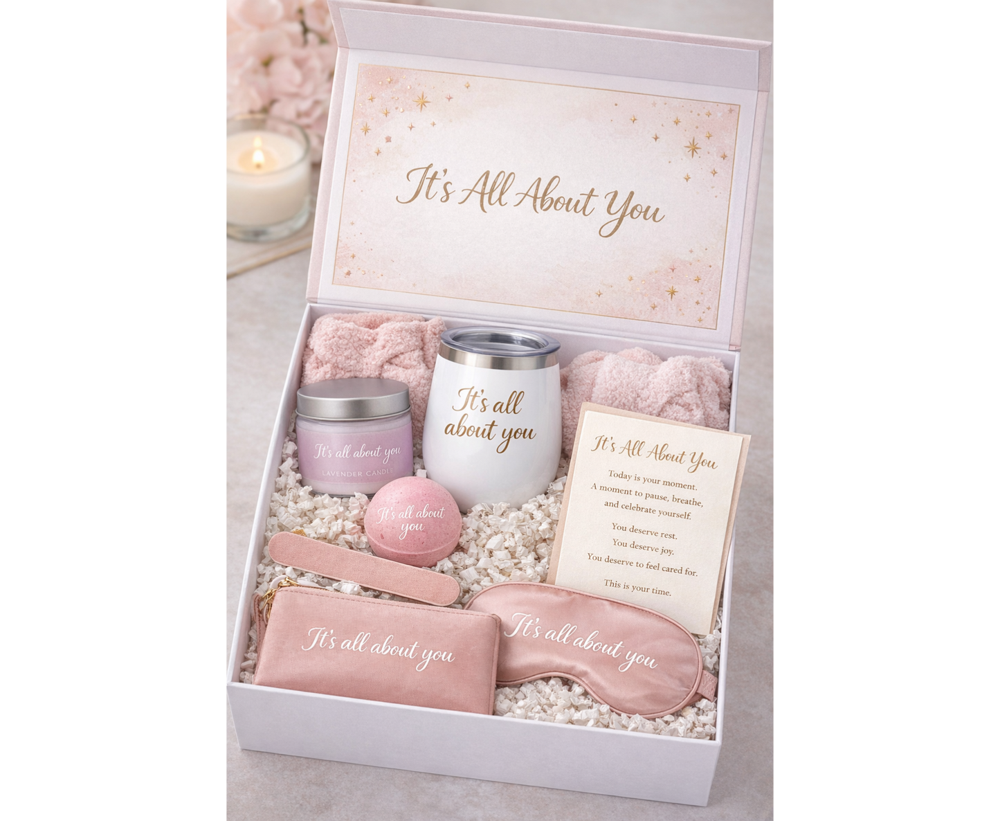 Gift set with pink items including a candle, eye mask, and card in a box labeled 'It's All About You'.
