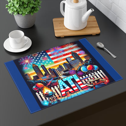 A vibrant Atlanta-themed placemat displayed on a black dining table with a teapot, cup, and spoon. The design features the Atlanta skyline with tall buildings, a large American flag, and colorful fireworks in the sky. The foreground includes BBQ grill flames, picnic tables, balloons, and bold "ATL" lettering with a stars and stripes pattern, making it perfect for 4th of July, summer parties, and Atlanta-themed décor.