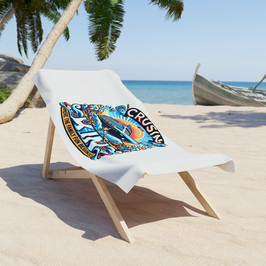 A white beach towel featuring a colorful "Cruising with Kin – Where the Family Fun Begins!" cruise ship graphic, draped over a wooden lounge chair on a tropical beach with palm trees, clear blue sky, and a boat in the background.