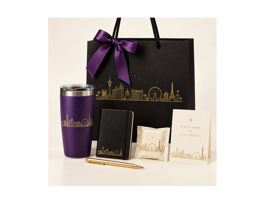 Black Las Vegas skyline gift bag with purple ribbon, purple tumbler, black journal, gold pen, wrapped treat, and welcome card.