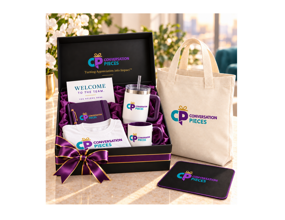 Conversation Pieces Premium welcome kit with a white branded T-shirt, purple notebook and pen, handled tumbler, coffee mug, and welcome card in a black satin-lined gift box, beside a linen-colored tote and branded mouse pad.