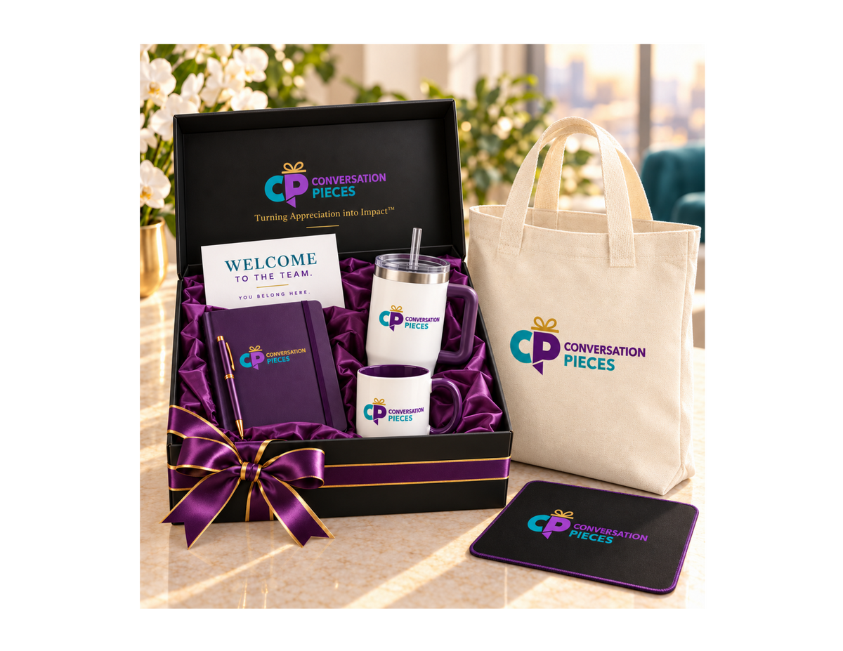 Conversation Pieces Premium welcome kit with notebook, pen, handled tumbler, coffee mug, welcome card, linen-colored tote, and mouse pad, displayed with a black gift box lined in purple satin and tied with purple-and-gold ribbon.