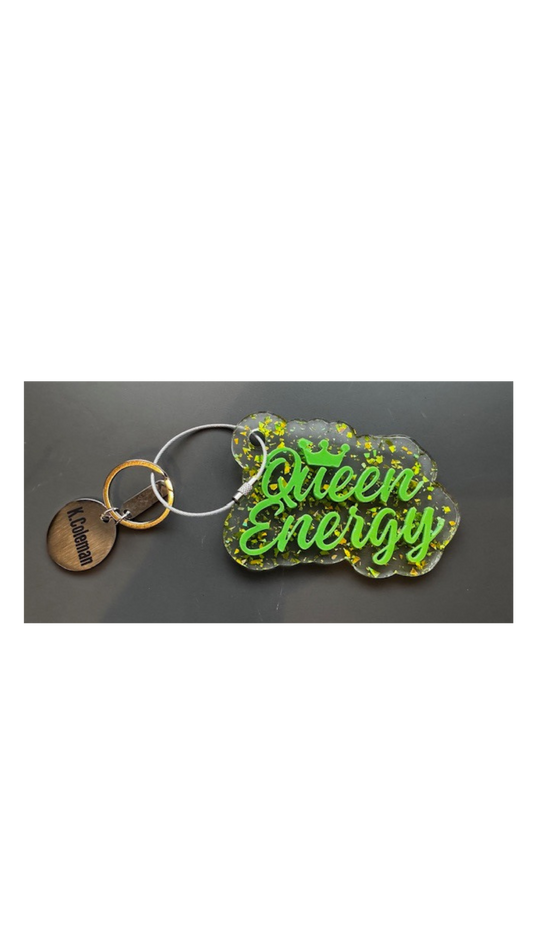 A green acrylic keychain with the text 'Queen Energy' written on it, displayed on a grey background.