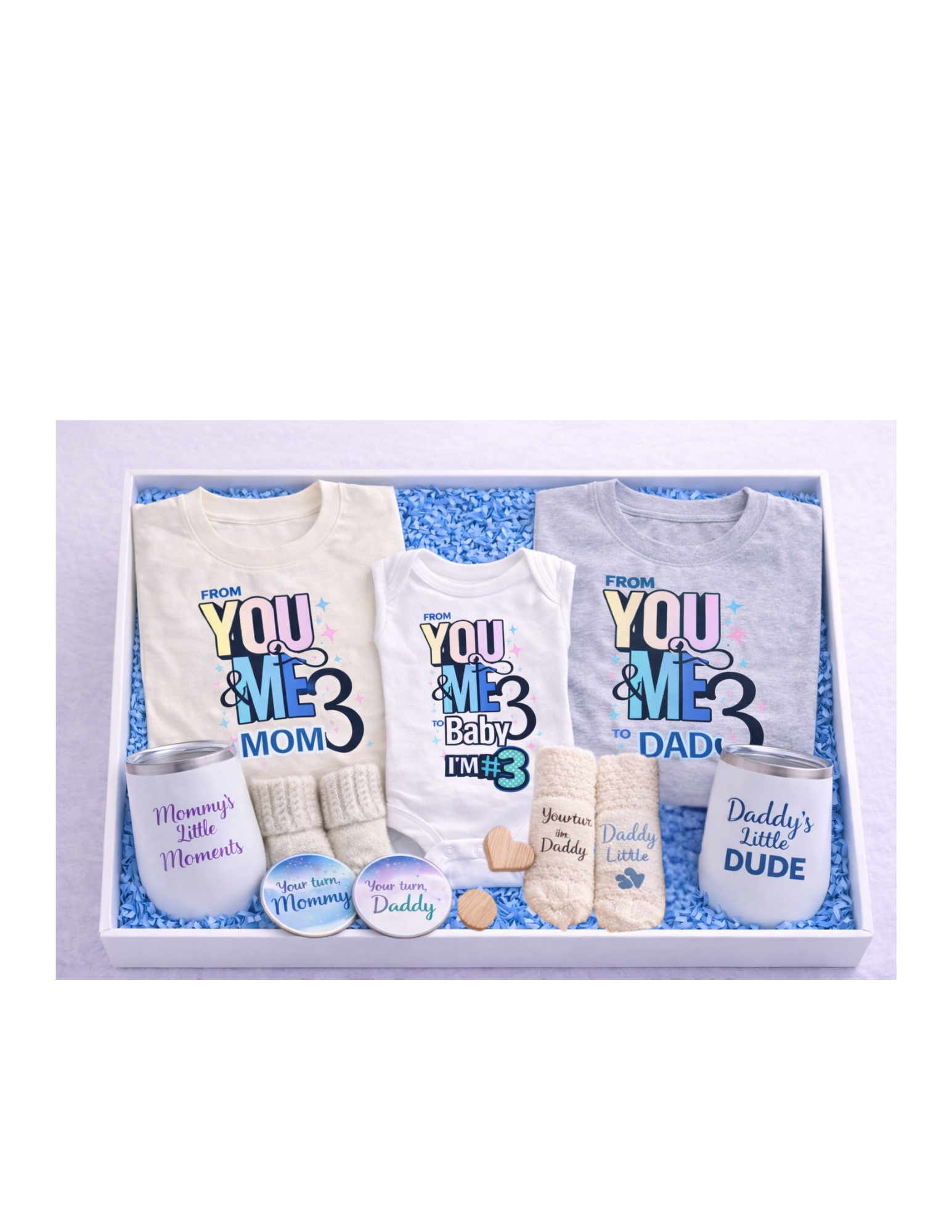 A curated family gift box in a white box with blue crinkle paper featuring matching “From You & Me to Us Three” shirts for mom and dad, a baby onesie, mommy and daddy wine tumblers, soft knit socks for mom, dad, and baby, and coordinating “Your turn Mommy” and “Your turn Daddy” coasters—perfect for baby announcements, showers, and new parent gifts.